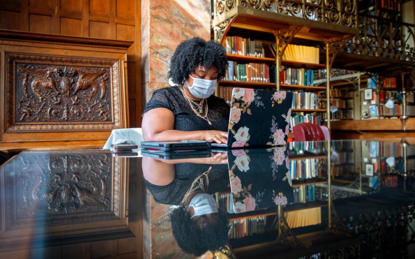 A student wearing a mask works in their reserved study space in the AD White Library