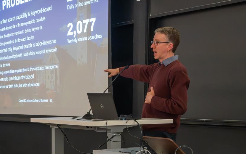 A presenter and projected slide during AI Demo Day; photo by Luke Stewart, Cornell- Bowers