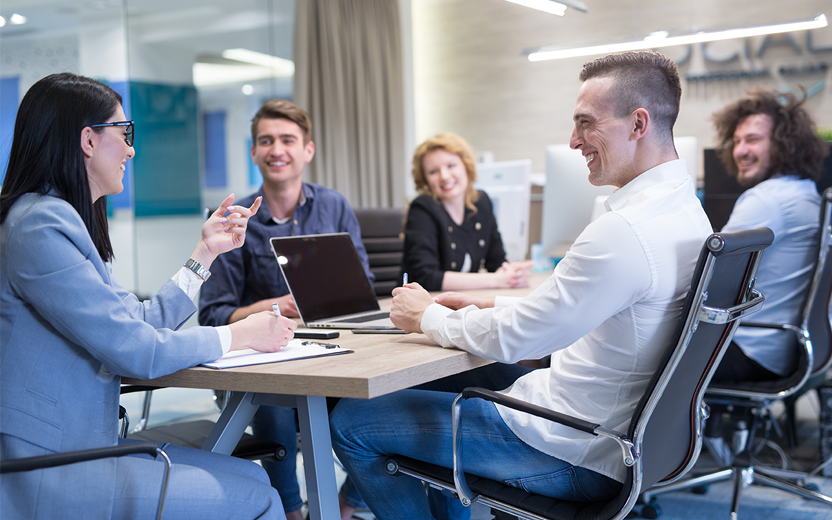 A group of professionals seated around a table, smiling and working together.