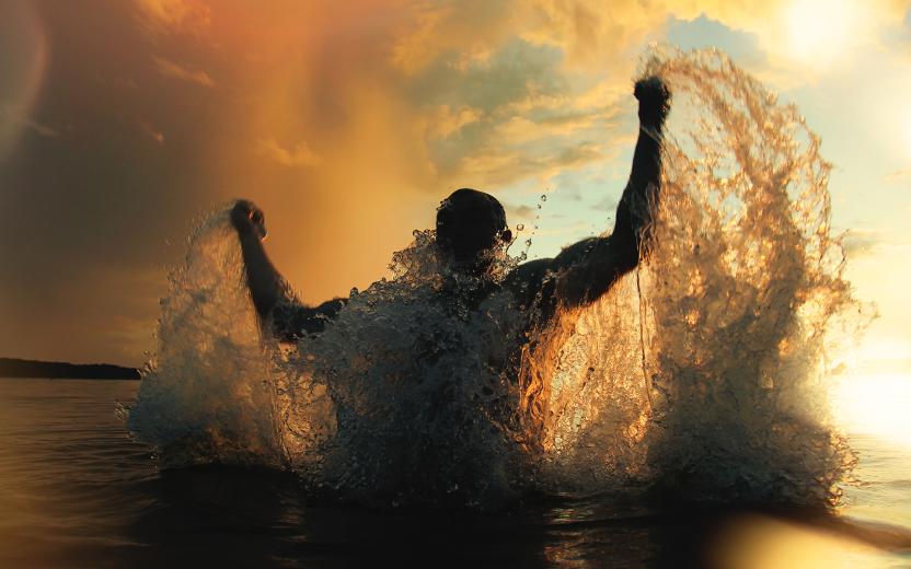 A triumphant swimmer leaps out of the water with fists raised in celebration