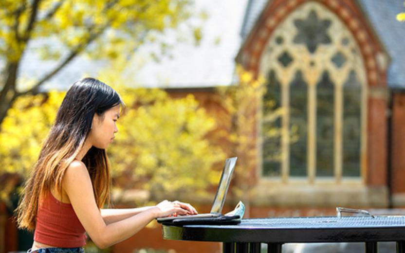 Student using computer in front of Sage Chapel