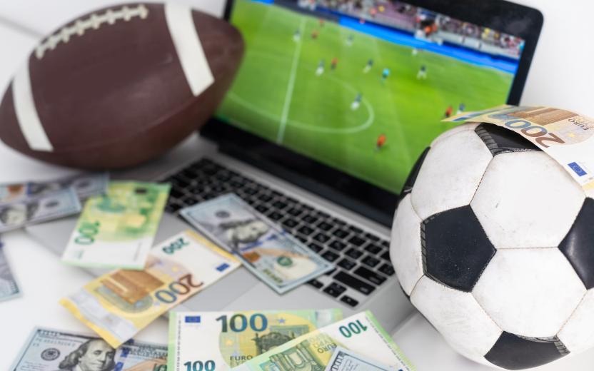 Adobe stock photo of sports balls, cash, and a laptop showing a US football game