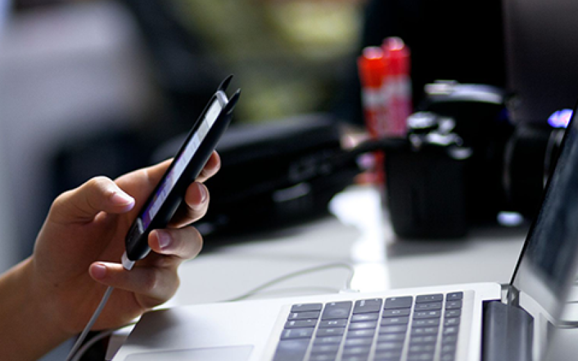 Student using smartphone with laptop at desk