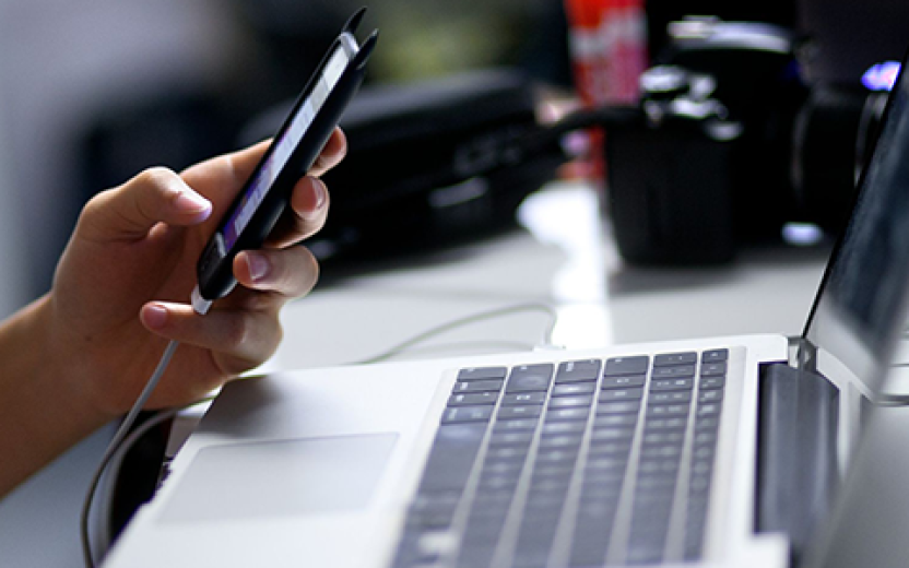 Student using smartphone with laptop at desk