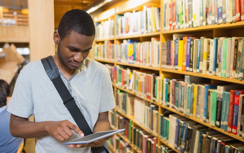 Student consulting tablet in library stacks.