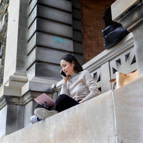A student works outside Sibley Hall using a laptop and phone