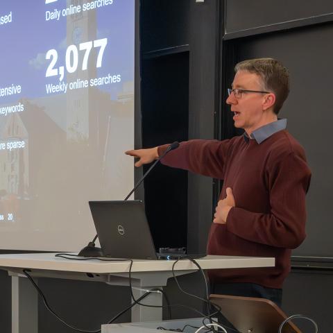 A presenter and projected slide during AI Demo Day; photo by Luke Stewart, Cornell- Bowers