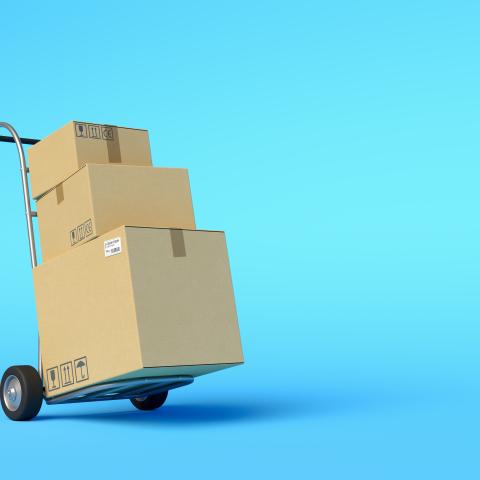 a handcart stacked with moving boxes rolls across a blue background