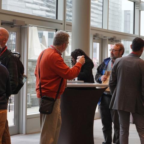 Small groups of co-workers stand around tall tables and converse over coffee