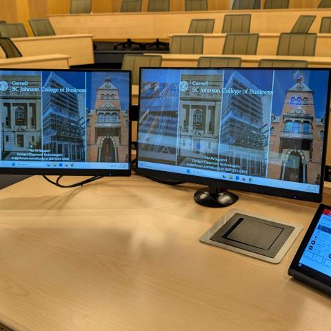 an instructor's desk with monitors and tablet displaying a new touch pad control interface for the clasroom technology
