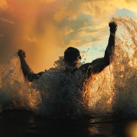 A triumphant swimmer leaps out of the water with fists raised in celebration