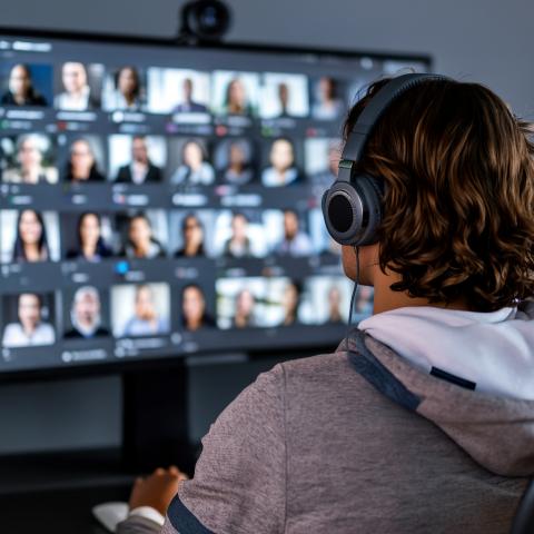 a man watches a videoconference discussion on a wide monitor