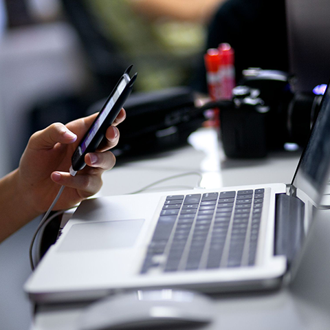 Student using smartphone with laptop at desk